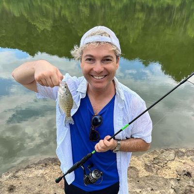 He is holding a fishing rod in one hand and a fish by its mouth is another.